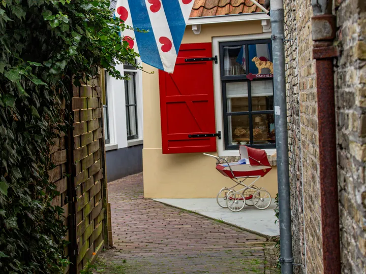 Een smalle steeg met de Friese vlag, rode luiken en een oude kinderwagen
